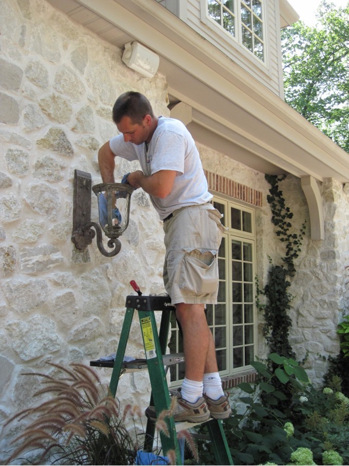 Man cleaning lights on outside of house